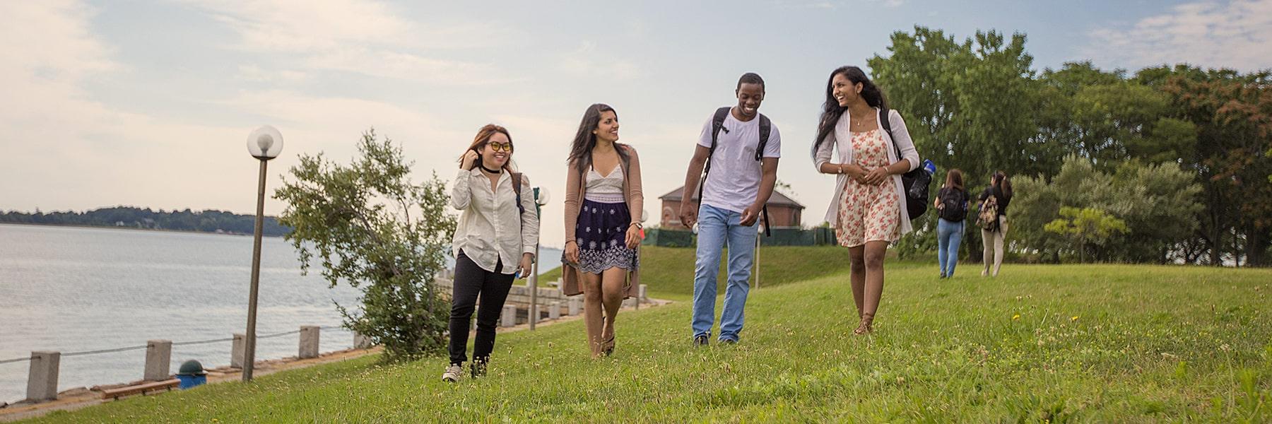 4 students walk along the lawn by the water.